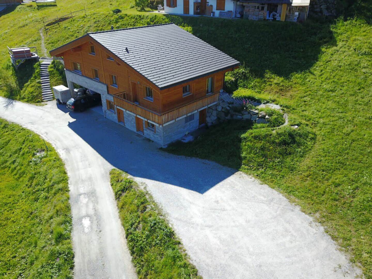 Aerial view of the chalet standing alone on a green alpine meadow