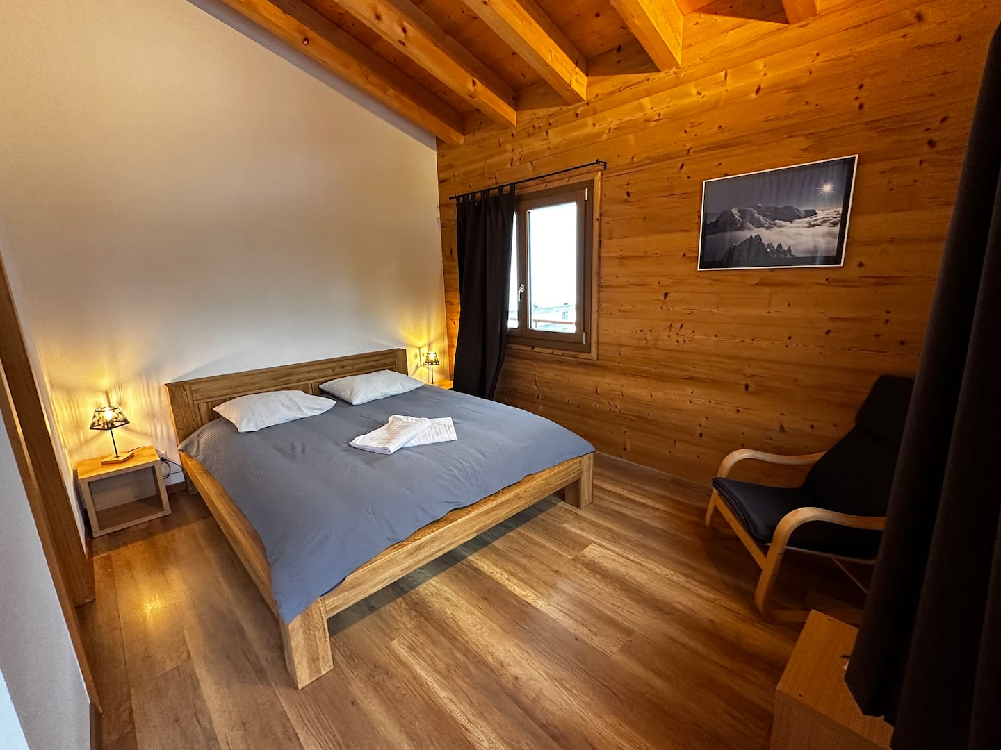Bedroom in the chalet with a wooden double bed and mountain photography on the wall